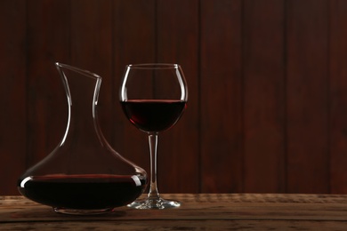 Photo of Elegant decanter and glass with red wine on table against dark background