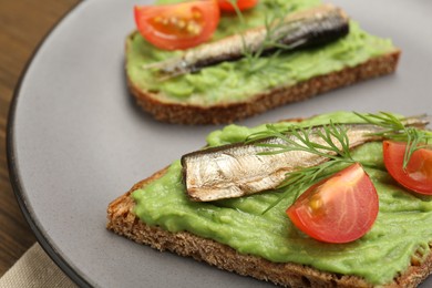 Photo of Delicious sandwiches with sprats, tomatoes, avocado puree and dill on wooden table, closeup