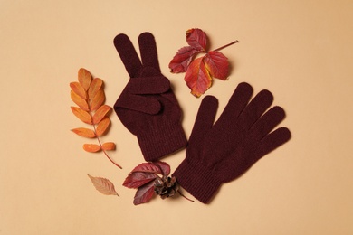 Stylish woolen gloves and dry leaves on beige background, flat lay