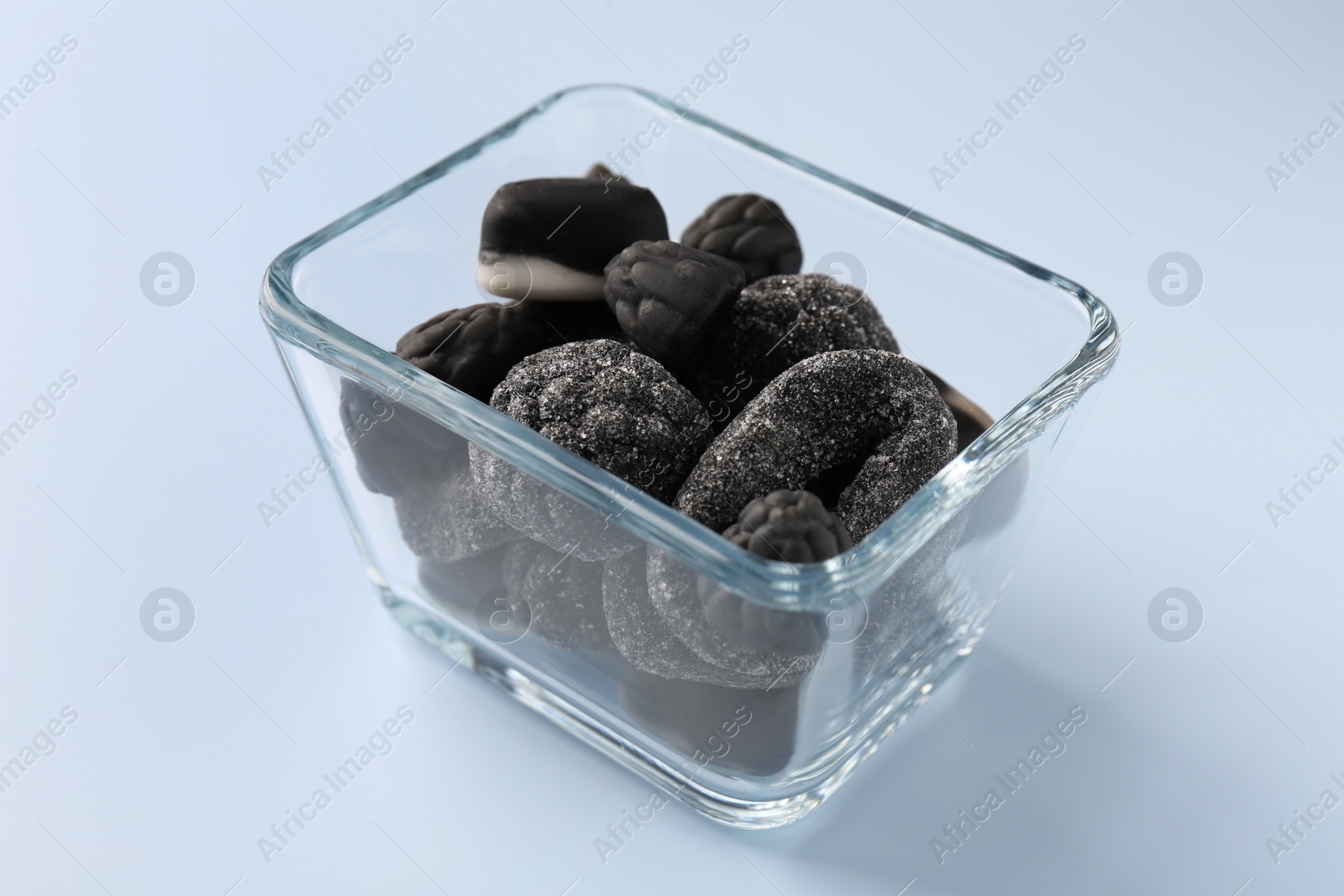 Photo of Glass container of tasty liquorice candies on light blue background