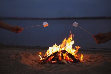 Photo of People roasting marshmallows over burning firewood on beach, closeup