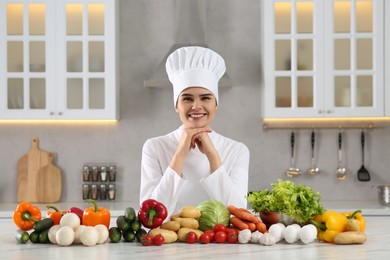 Portrait of happy chef near fresh vegetables at white marble table in kitchen