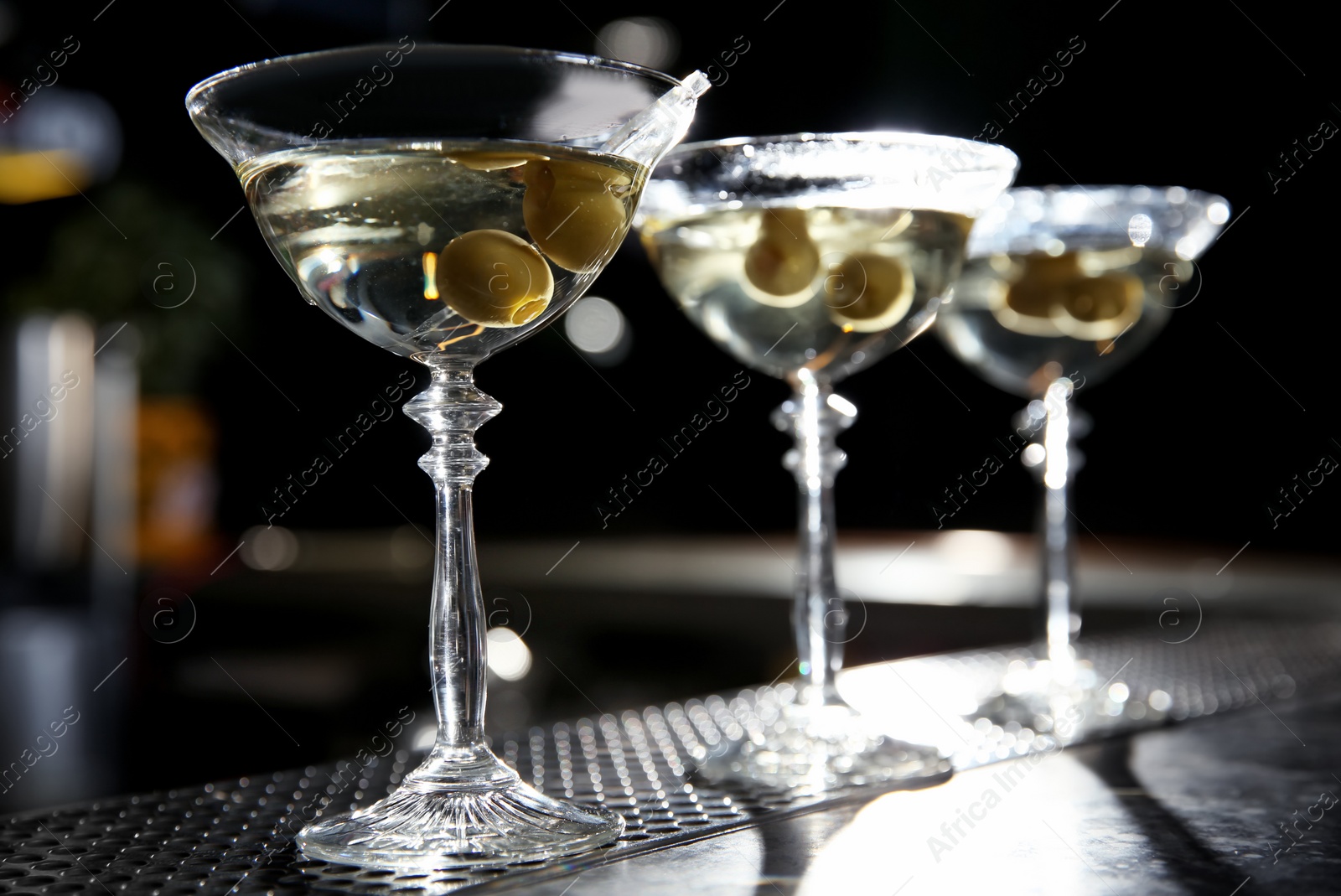 Photo of Glasses of martini cocktail with olives on bar counter. Space for text