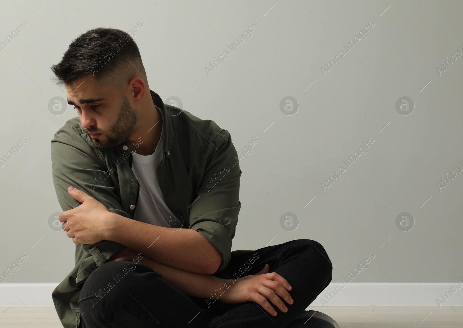 Photo of Sad man sitting near light grey wall. Space for text