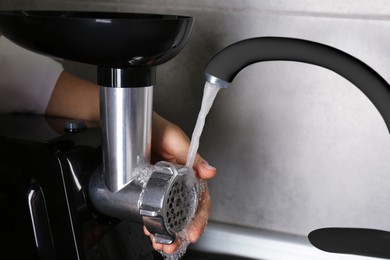 Photo of Woman washing electric meat grinder under tap water  indoors, closeup
