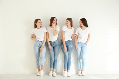 Beautiful young ladies in jeans and white t-shirts near light wall indoors. Woman's Day