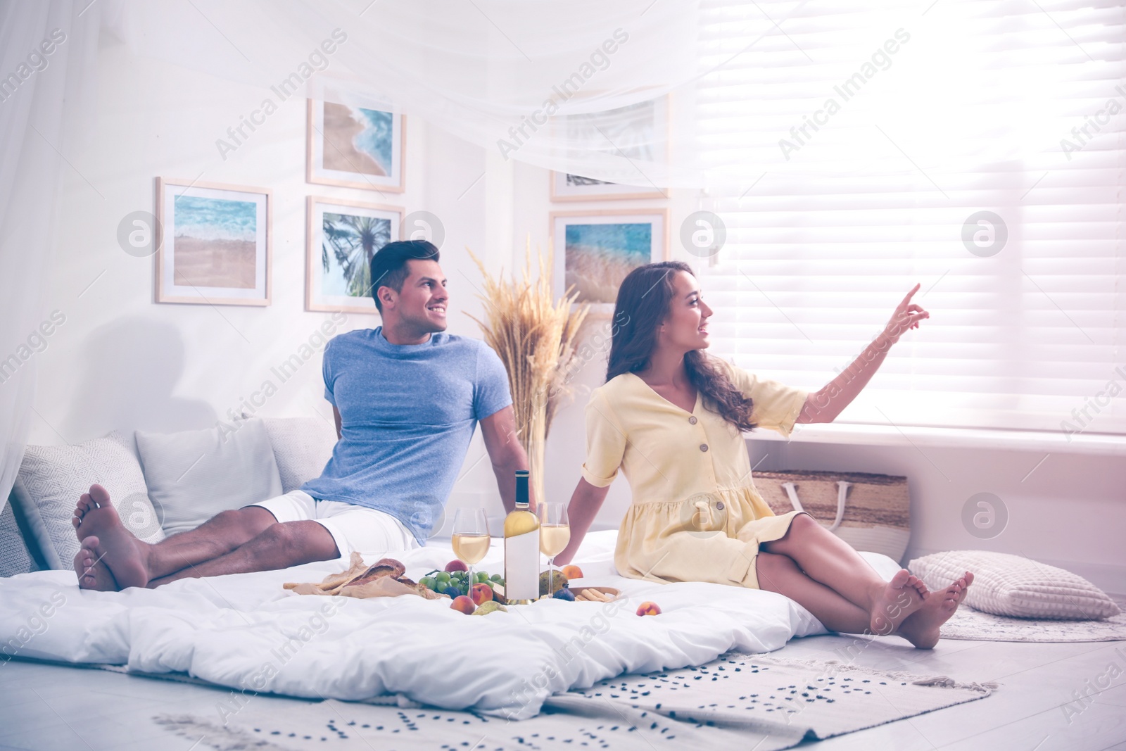 Photo of Happy couple with wine and tasty food imitating picnic at home