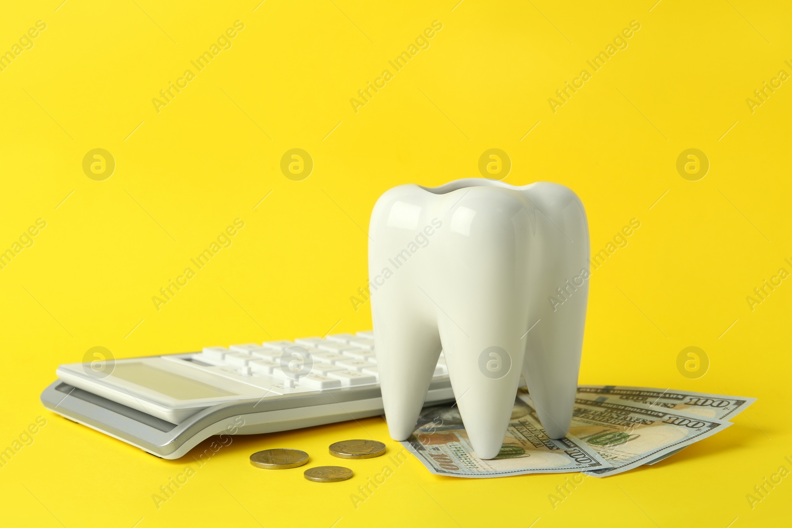 Photo of Ceramic model of tooth, money and calculator on yellow background. Expensive treatment