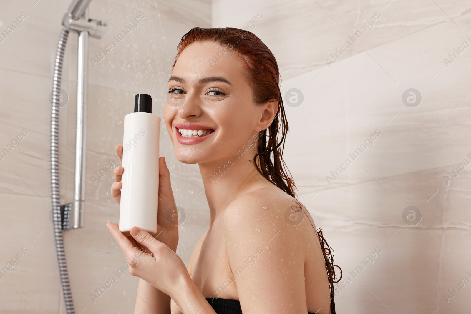 Photo of Happy young woman with bottle of shampoo in shower