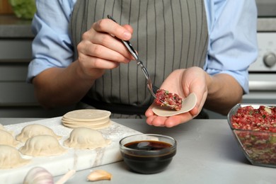 Photo of Woman putting gyoza filling in center of dough wrapper at light grey table, closeup