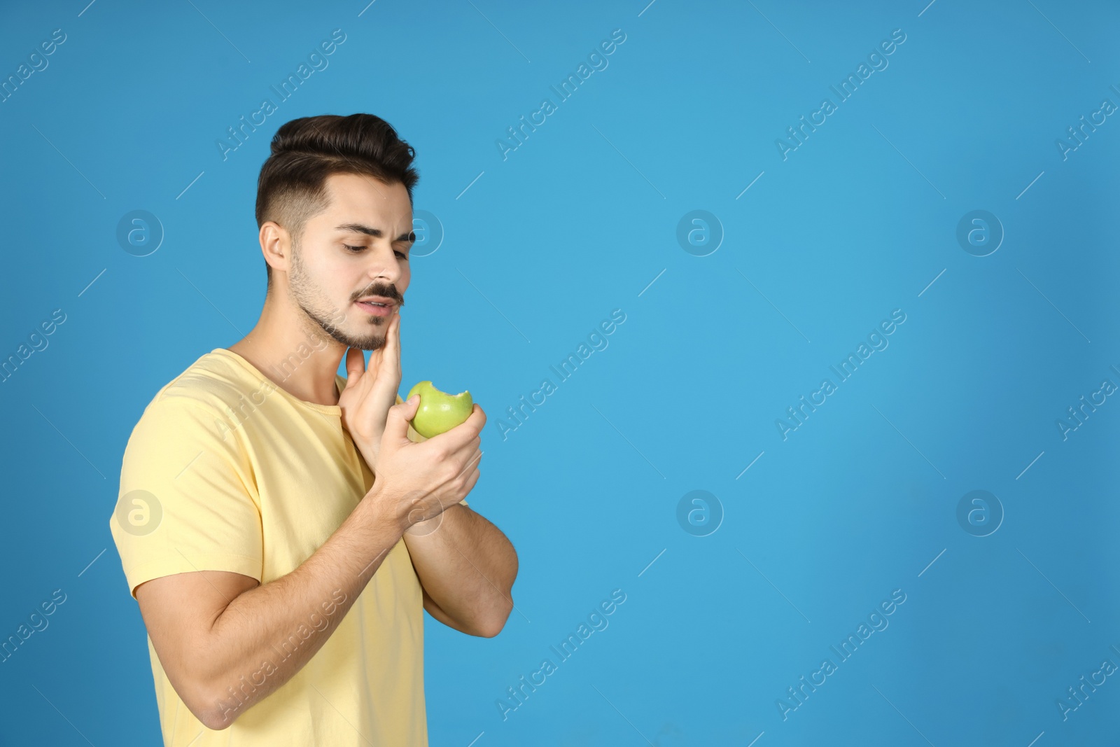 Photo of Young man with sensitive teeth and apple on color background. Space for text