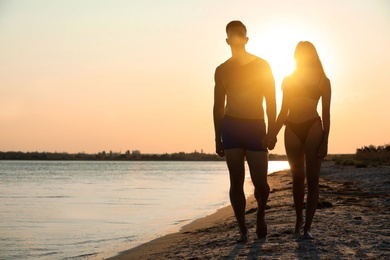 Photo of Young woman in bikini spending time with her boyfriend on beach at sunset. Lovely couple