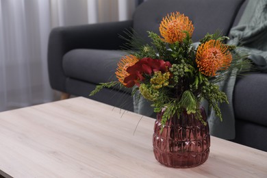 Vase with bouquet of beautiful leucospermum flowers on wooden table in living room, space for text