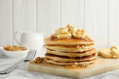 Photo of Delicious pancakes with bananas, walnuts and honey on white marble table, closeup