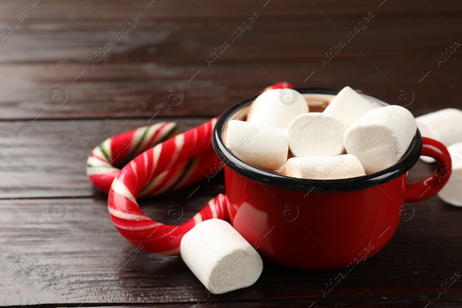 Photo of Tasty hot chocolate with marshmallows and candy cane on wooden table, closeup. Space for text