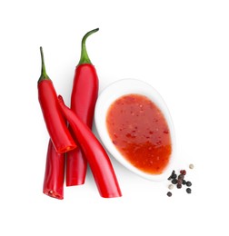 Photo of Spicy chili sauce, peppers and peppercorns isolated on white, top view