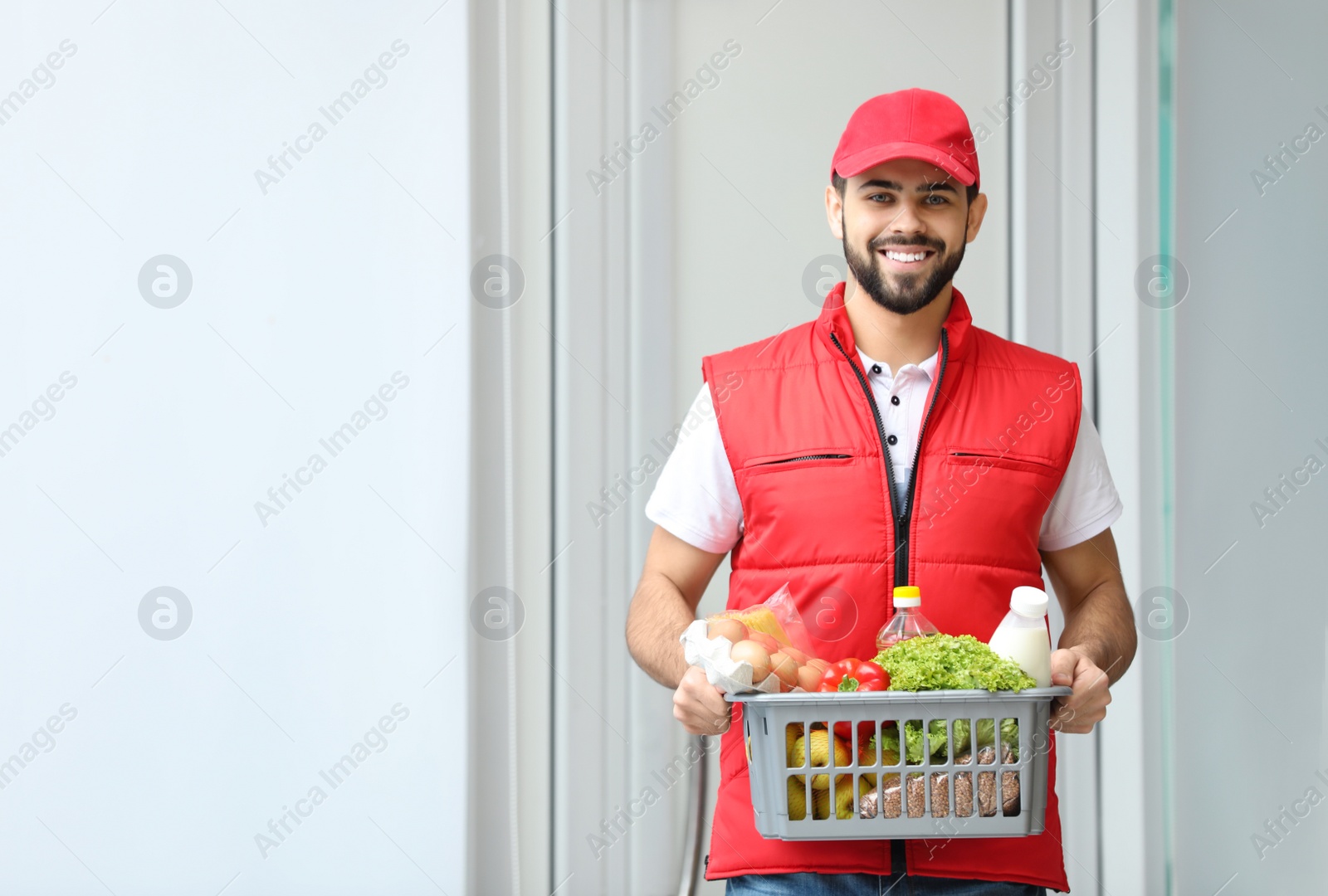 Photo of Man holding basket with fresh products near entrance, space for text. Food delivery service