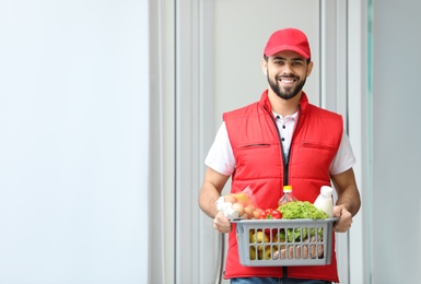 Man holding basket with fresh products near entrance, space for text. Food delivery service