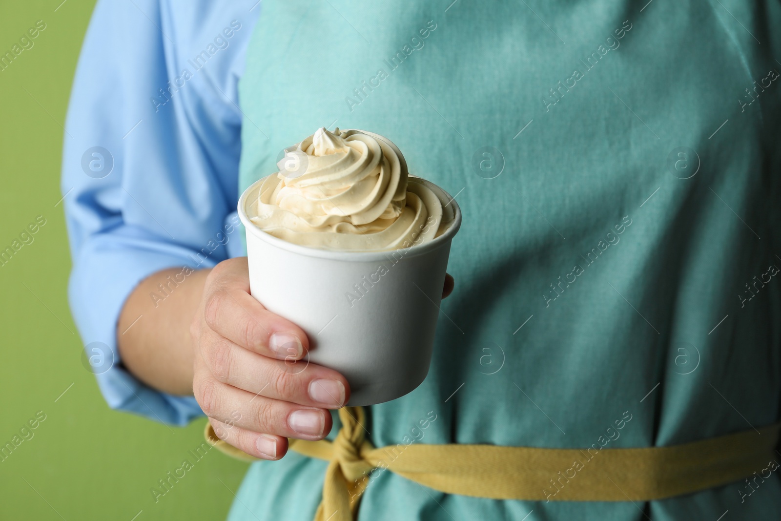 Photo of Woman holding cup with tasty frozen yogurt on green background, closeup