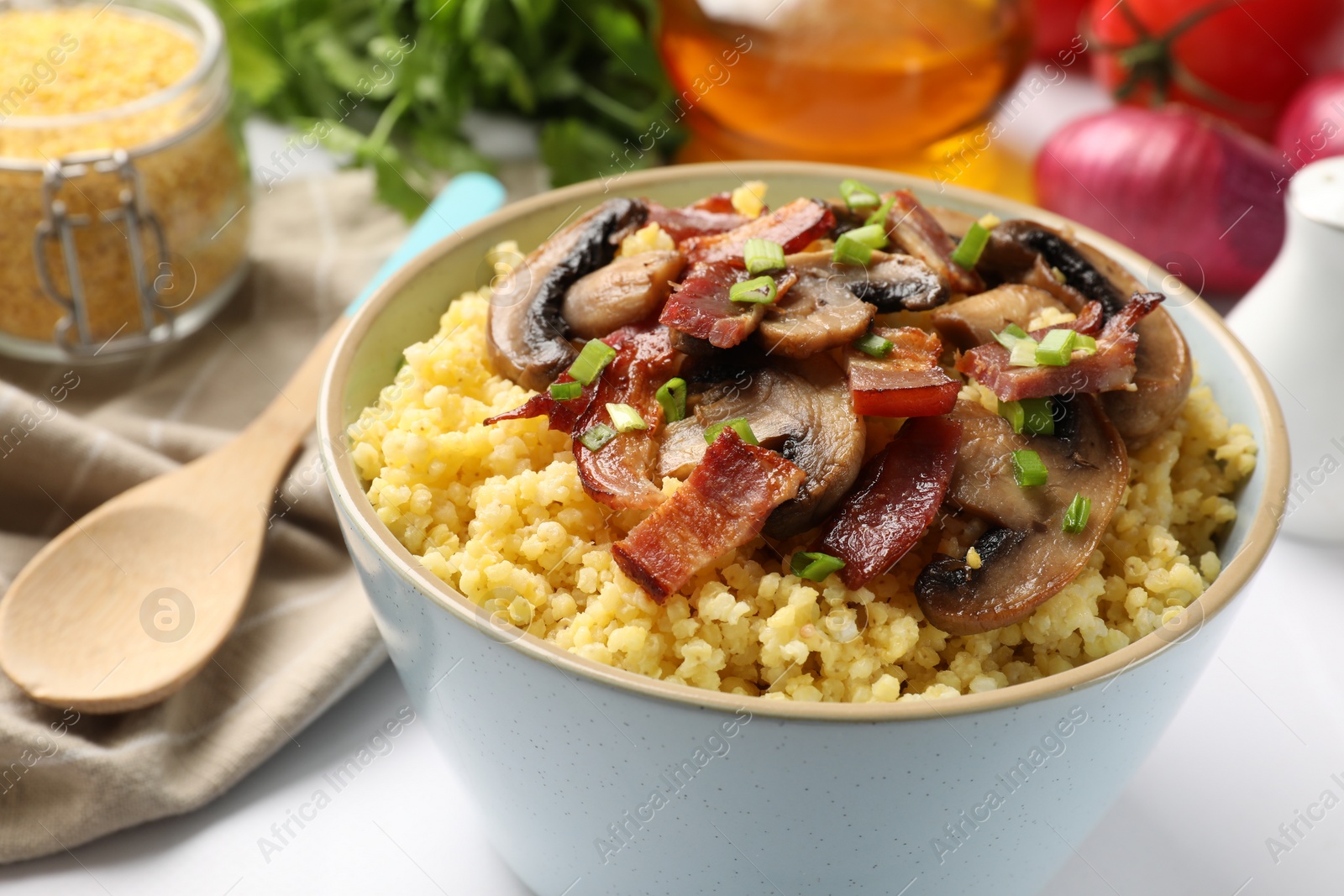 Photo of Tasty millet porridge with mushrooms, bacon and green onion in bowl on white table, closeup