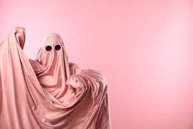 Photo of Glamorous ghost. Woman in sheet with sunglasses on pink background, space for text