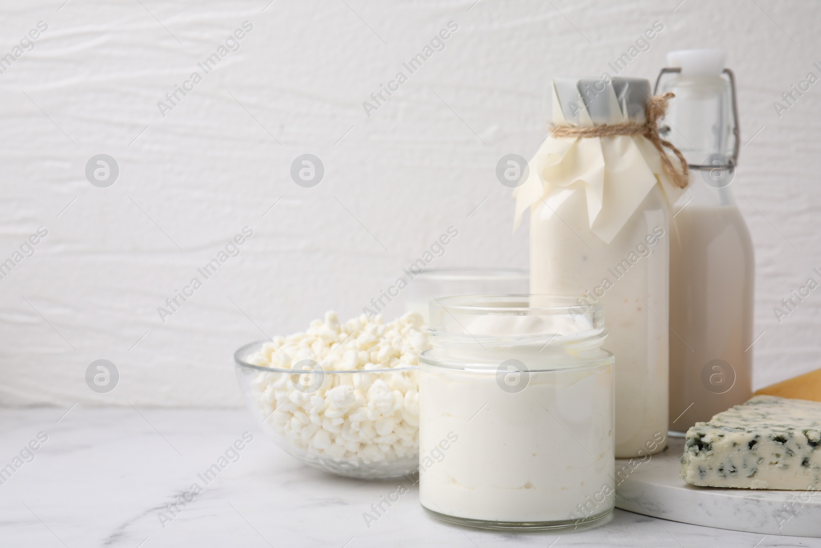 Photo of Different fresh dairy products on white marble table, space for text