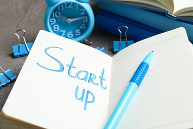 Photo of Notebook with phrase Start Up and pen on grey table, closeup