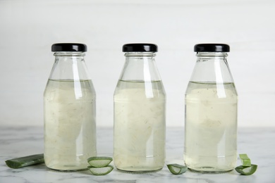 Photo of Fresh aloe drink in bottles and leaf slices on white marble table