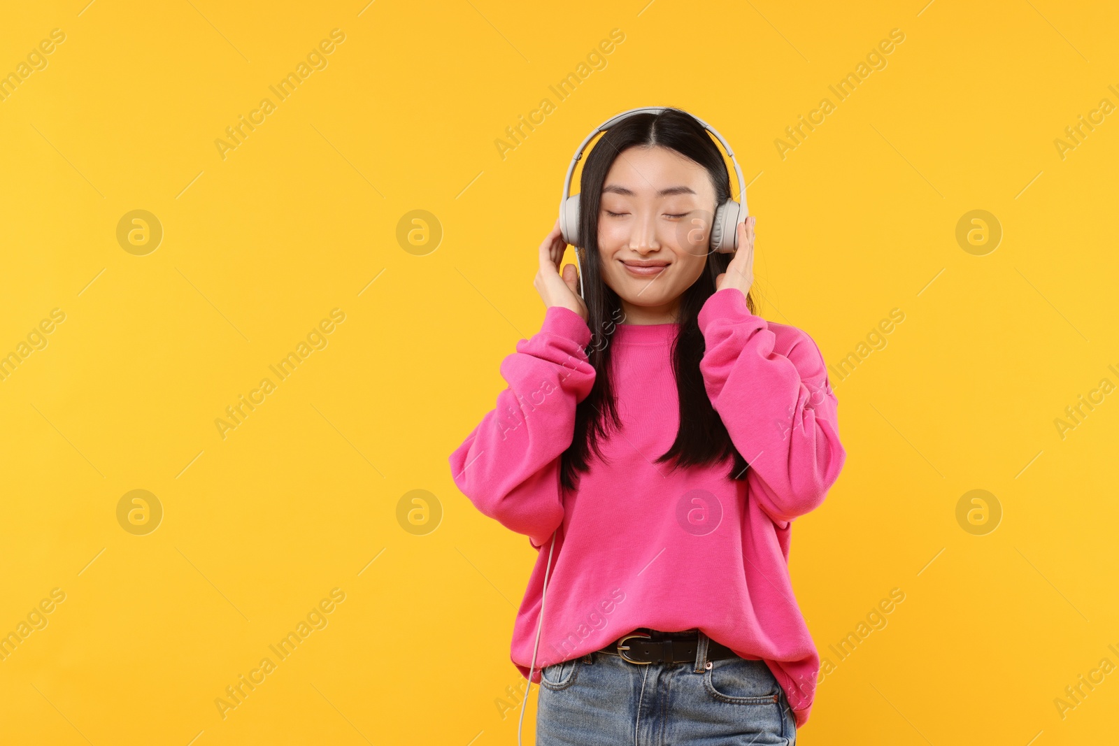 Photo of Portrait of beautiful woman in headphones on orange background. Space for text