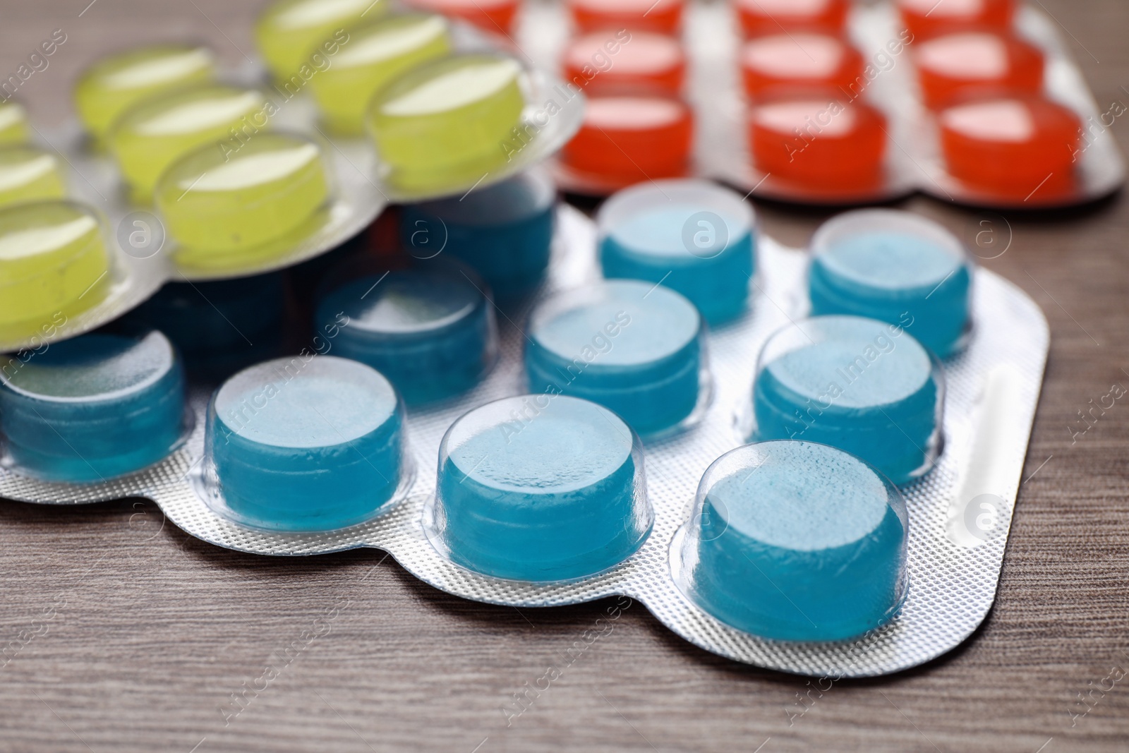 Photo of Blisters with colorful cough drops on wooden background, closeup