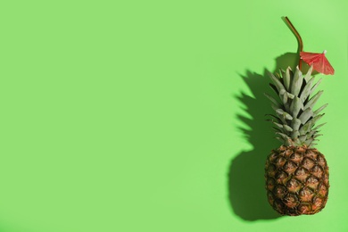 Photo of Creative composition with pineapple, straw and cocktail umbrella on green background. Space for text