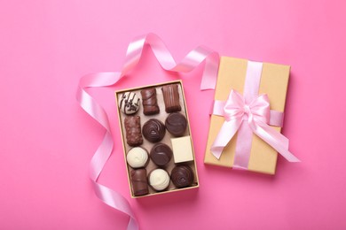 Photo of Open box with delicious chocolate candies and ribbon on pink background, top view