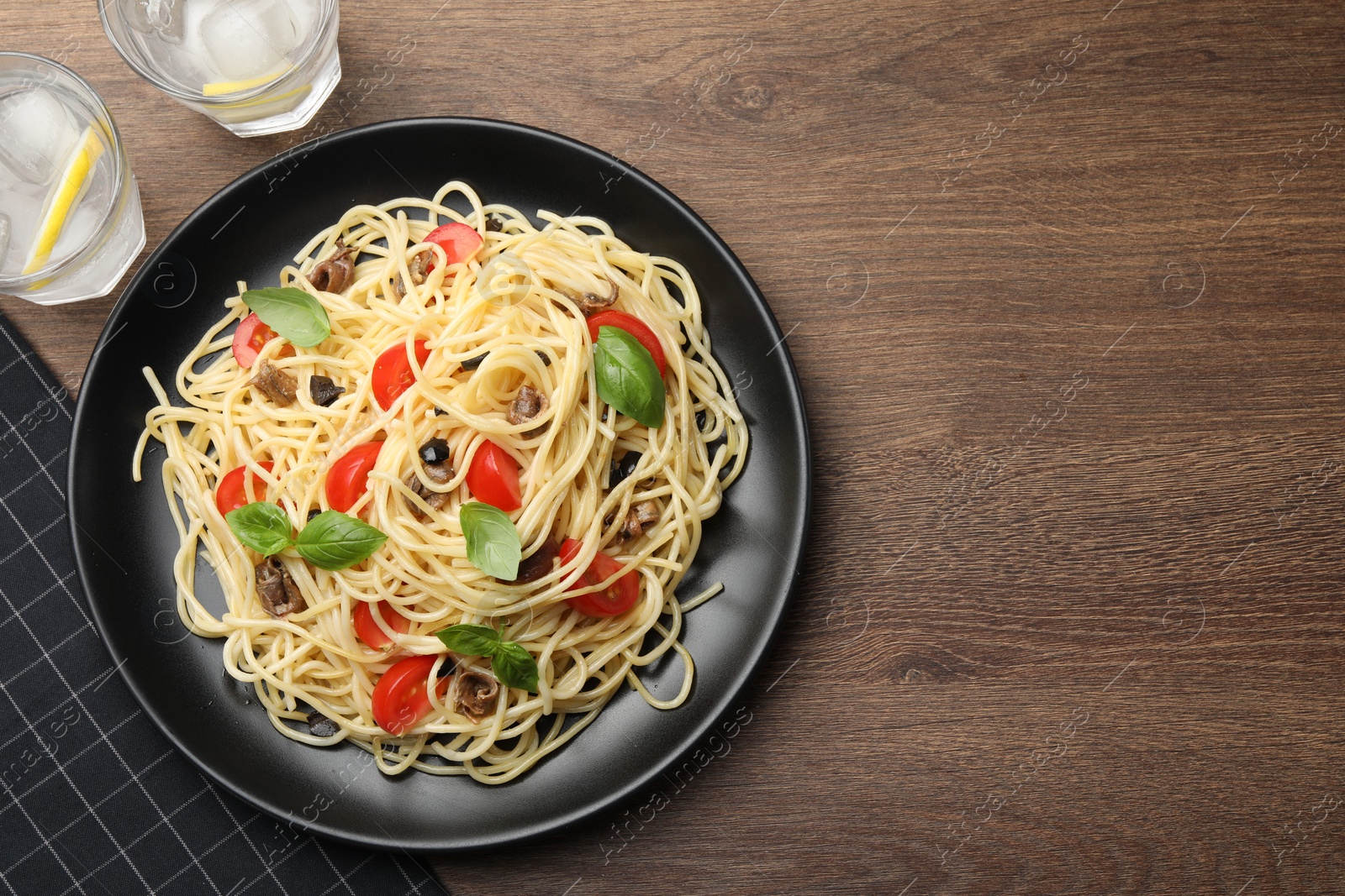 Photo of Delicious pasta with anchovies, tomatoes and glasses of beverage on wooden table, flat lay. Space for text