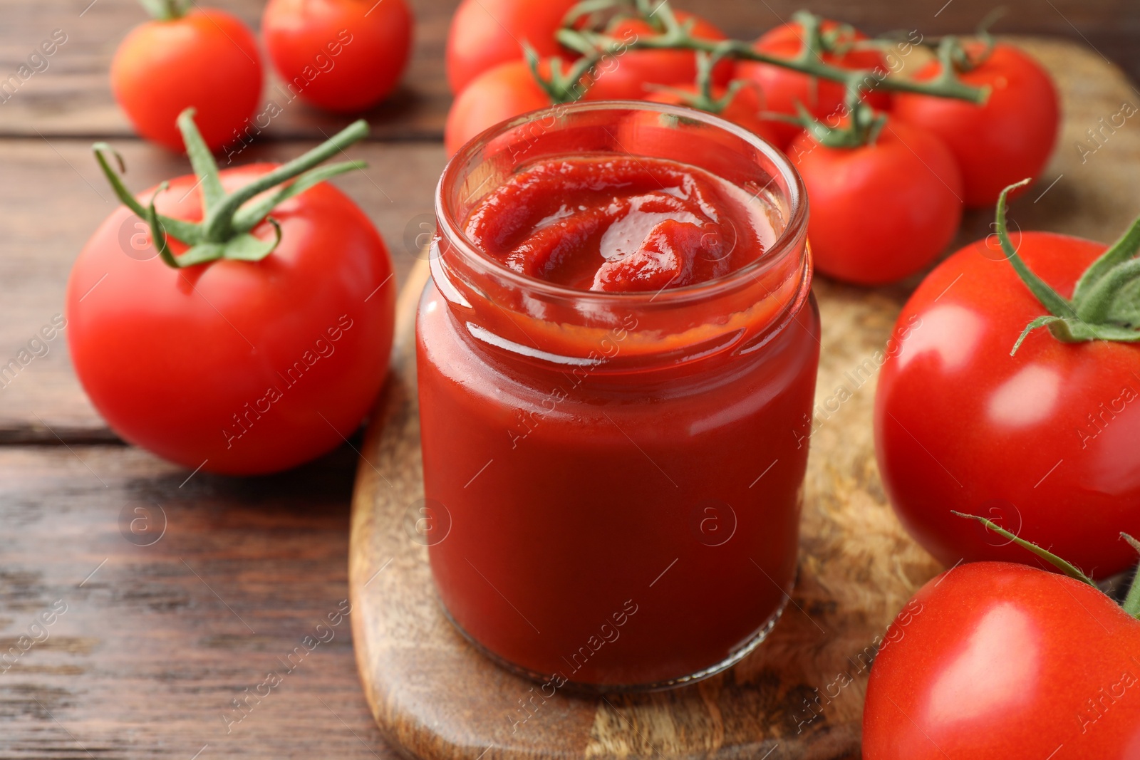 Photo of Jar of tasty ketchup and tomatoes on wooden table, closeup