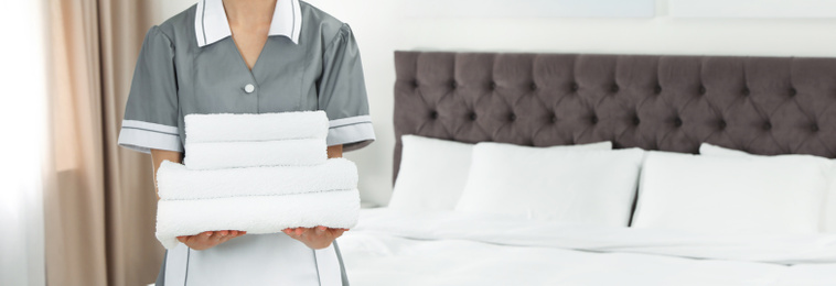 Chambermaid holding stack of fresh towels in hotel room, closeup view with space for text. Banner design