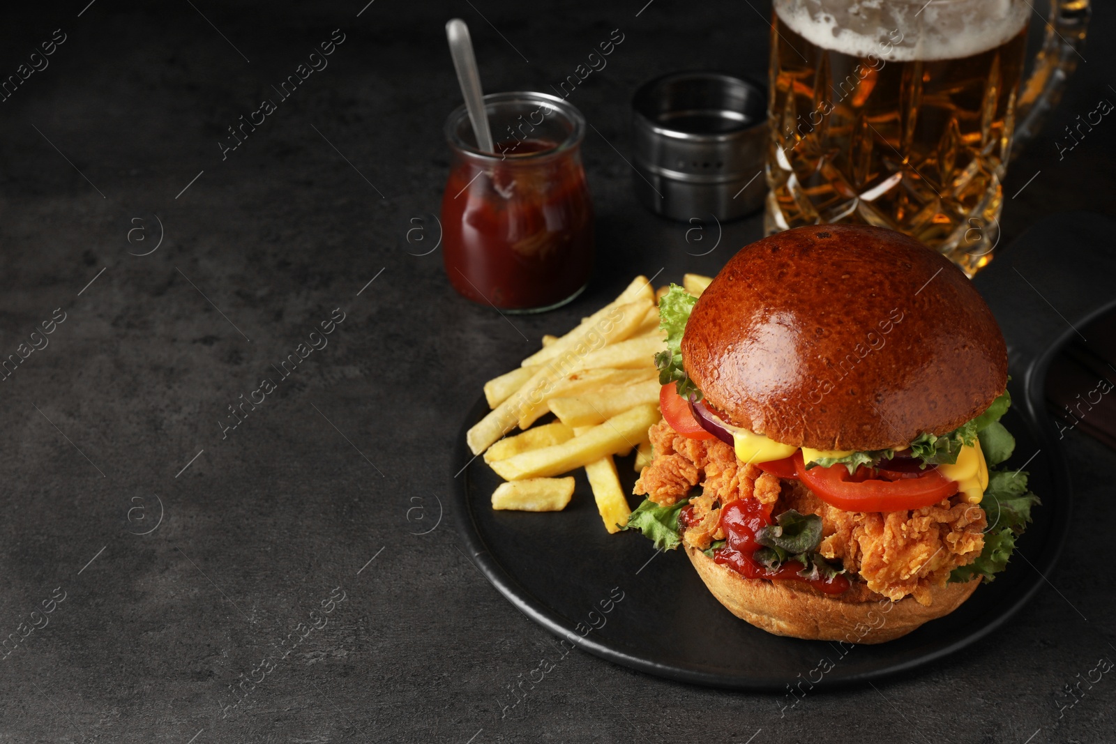 Photo of Delicious burger with crispy chicken patty, french fries, sauce and beer on black table. Space for text