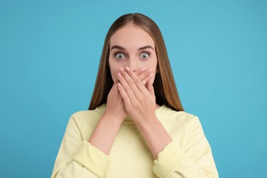 Photo of Embarrassed woman covering mouth with hands on light blue background