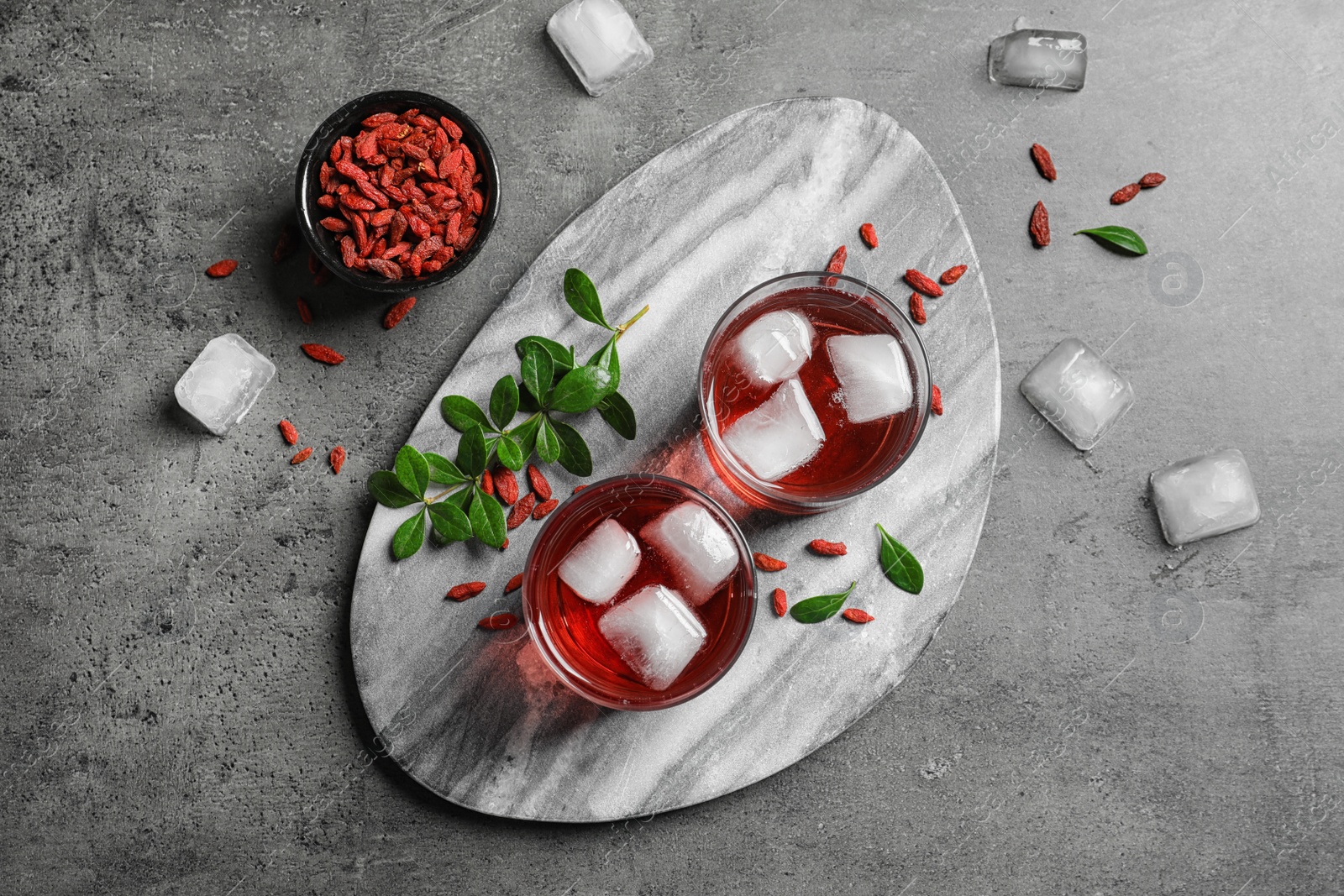 Photo of Healthy goji juice in glasses served on grey table, flat lay