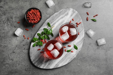 Photo of Healthy goji juice in glasses served on grey table, flat lay