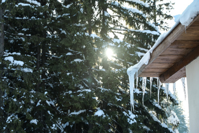 Photo of Wooden house with icicles near snowy forest. Winter vacation