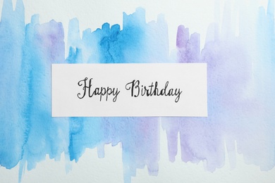 Photo of Card with words HAPPY BIRTHDAY on watercolor painting, top view