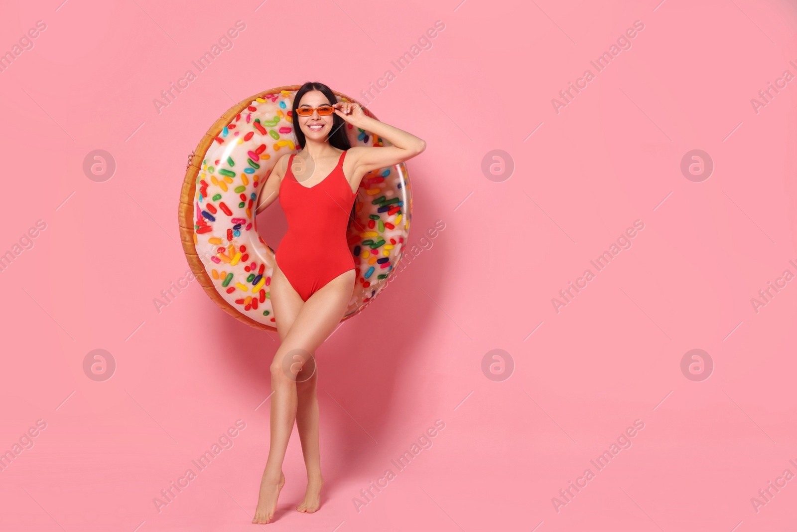 Photo of Young woman with stylish sunglasses holding inflatable ring against pink background