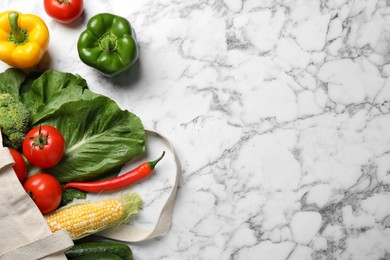 Photo of Cloth bag with different fresh vegetables on white marble table, flat lay. Space for text