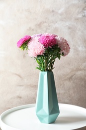 Beautiful aster flower bouquet in vase on table against color background