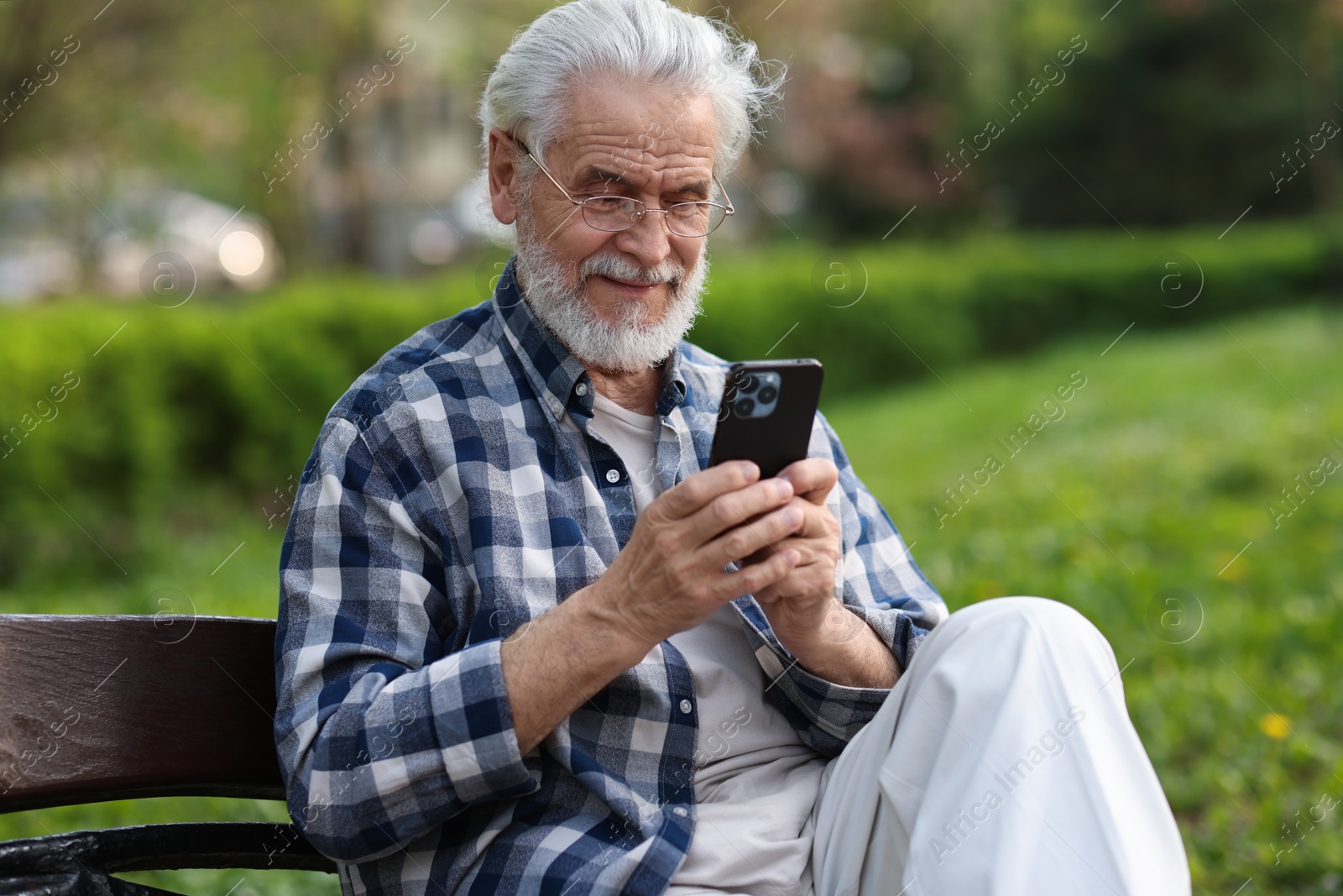 Photo of Portrait of happy grandpa with glasses using smartphone on bench in park