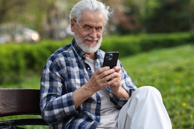 Portrait of happy grandpa with glasses using smartphone on bench in park
