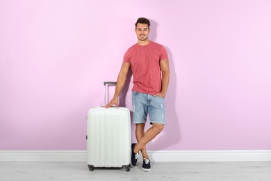 Young man with suitcase on color wall background