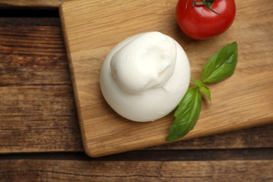 Photo of Delicious burrata cheese with basil and cherry tomato on wooden table, top view