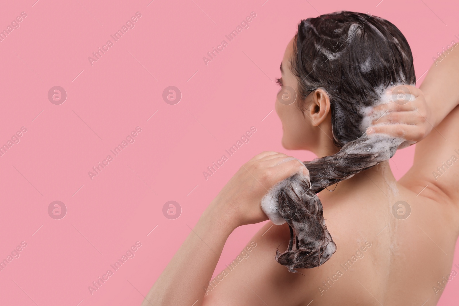 Photo of Woman washing hair on pink background, back view. Space for text