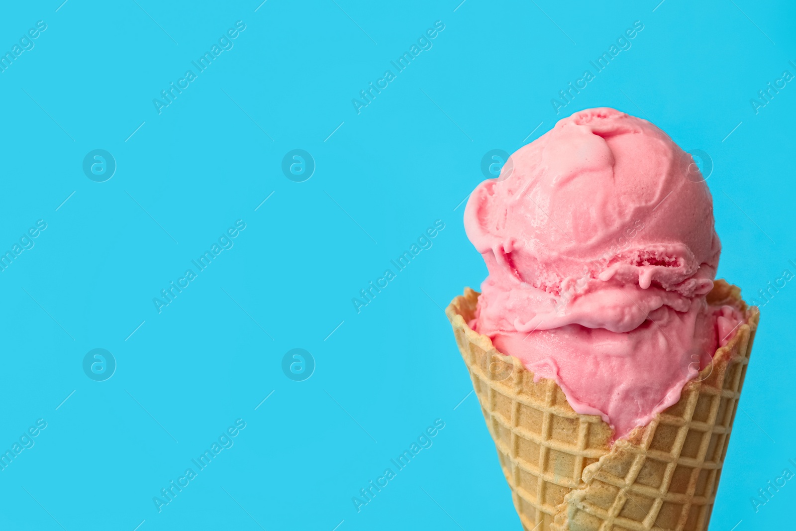 Photo of Delicious pink ice cream in waffle cone on light blue background, closeup. Space for text